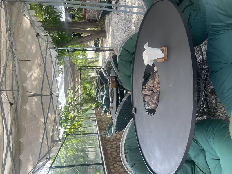 فضای باز باغ رستوران کیافود با میزهای آتشدان، صندلی‌های راحت سبز و سقف‌های سایه‌بان، محیطی دلنشین و آرامش‌بخش برای مشتریان.