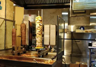 آشپزخانه فست فود فرید با سه سیخ کباب ترکی دونر و شاورما در حال پخت، محیطی تمیز برای آماده‌سازی غذاهای سریع و خوشمزه.