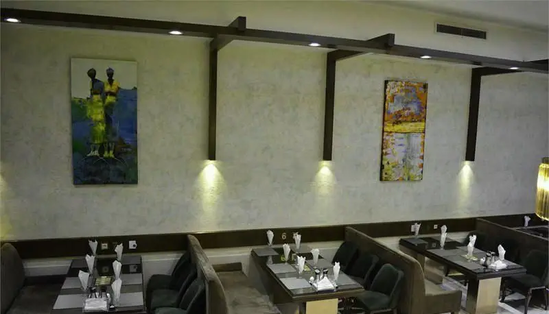 رستوران ایرانی سانلی: دکوراسیون داخلی شیک و مدرن با میزهای چیده شده، نورپردازی گرم و نقاشی‌های دیواری. فضایی دلنشین برای صرف غذا.