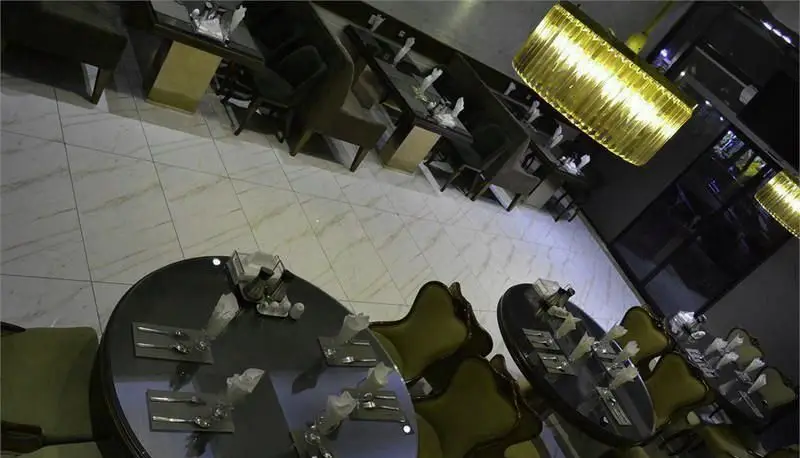 نمای داخلی رستوران ایرانی سانلی با میزهای گرد و مربع چیده شده، صندلی‌های راحت و نورپردازی طلایی، محیطی آرامش‌بخش برای مشتریان.