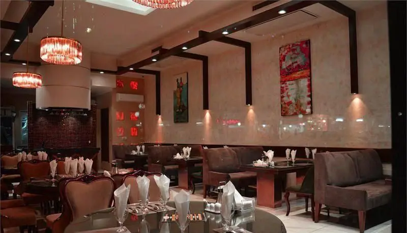 فضای داخلی دلنشین رستوران ایرانی سانلی با دکوراسیون مدرن و لوکس. میزهای چیدمان شده، صندلی‌های راحت، لوستر و نورپردازی گرم.