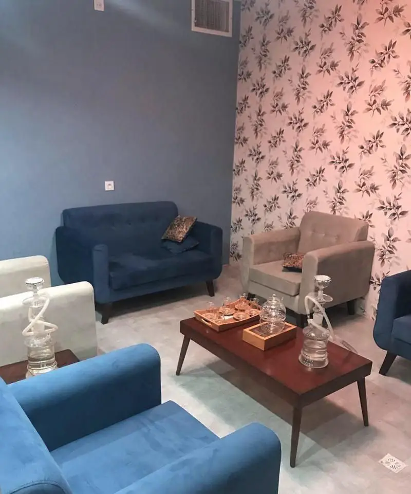 فضای داخلی کافی شاپ باربتا با دکوراسیون شیک، شامل دیوارهای آبی و کاغذ دیواری گلدار، مبلمان آبی و بژ، میز پذیرایی چوبی با قلیان و چای.