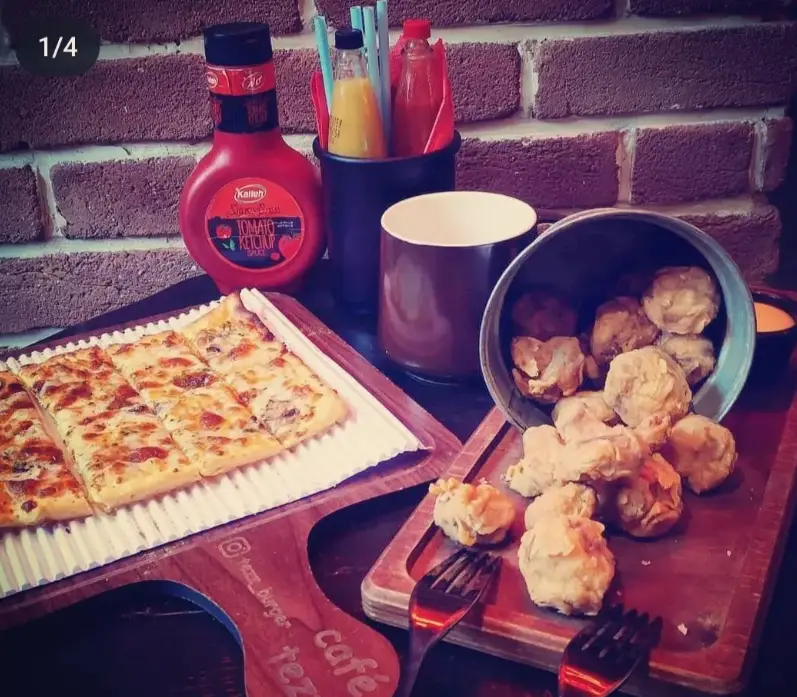 نمای جذاب از میز غذای کافه تز شامل پیتزا مستطیلی، قارچ سوخاری ترد، کچاپ کاله و فضای دلنشین با آجرکاری. لذت طعم اصیل.