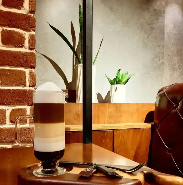 یک فنجان قهوه لایه ای ماکیاتو در فضای دنج و دلنشین کافه تز. لذت نوشیدن یک قهوه گرم در محیطی آرام.