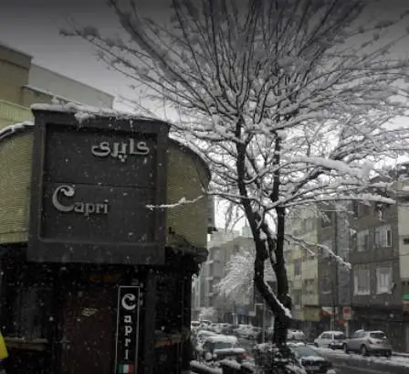 تصویری زیبا و برفی از نمای بیرونی رستوران ایتالیایی کاپری در یک روز زمستانی. تابلوی نام "Capri" به فارسی و انگلیسی بر فراز ساختمان.