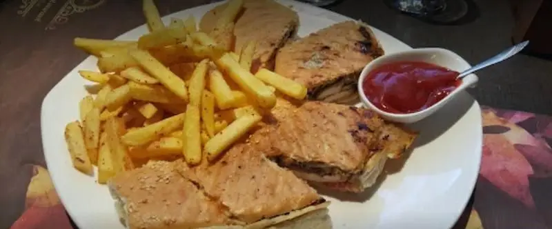 تصویری از یک بشقاب غذای لذیذ شامل پیتزا ساندویچ یا پانینی گریل شده، سیب زمینی سرخ کرده و سس کچاپ در رستوران ایتالیایی کاپری.