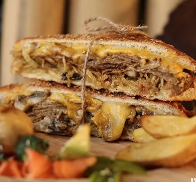 ساندویچ حجیم گریل شده استیک گوشت با پنیر ذوب شده و پیاز کاراملی از کافه رستوران رولینجا، همراه سیب زمینی وِج.