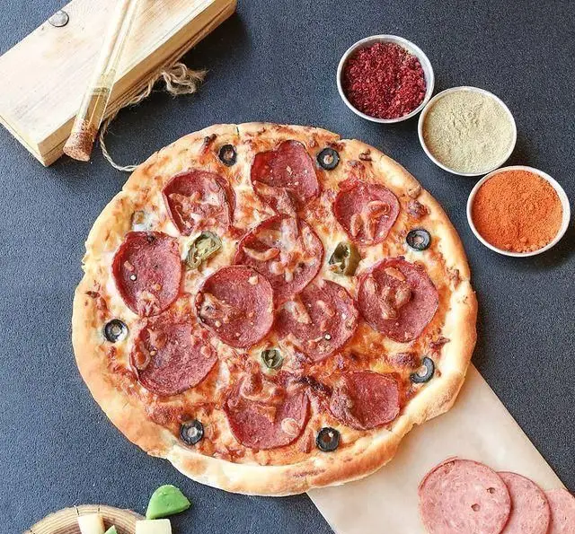 تصویری از یک پیتزا پپرونی لذیذ و پرملات کافه رستوران رولینجا، مزین به زیتون و فلفل هالوپینو، همراه ادویه‌ها و سوسیس.