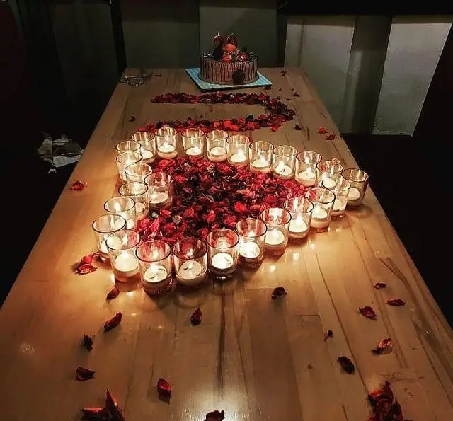 جشن تولد یا سالگرد خاص در کافه رستوران رولینجا: میز آرایی رمانتیک با شمع‌های درخشان، گلبرگ‌های رز قرمز و کیک شکلاتی.