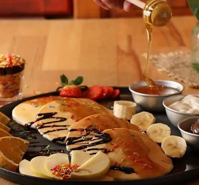 پنکیک‌های خوشمزه کافه رستوران رولینجا با عسل، شکلات و میوه‌های تازه (توت فرنگی، موز، پرتقال، سیب) یک صبحانه رویایی.
