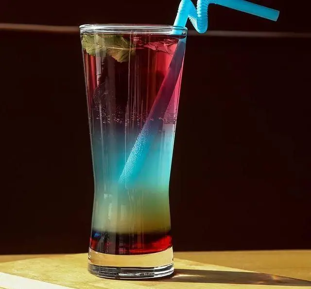 کوکتل رنگین‌کمان و خنک کافه رستوران رولینجا، لایه‌های قرمز، آبی و سبز با برگ نعنا و نی آبی در لیوان بلند.