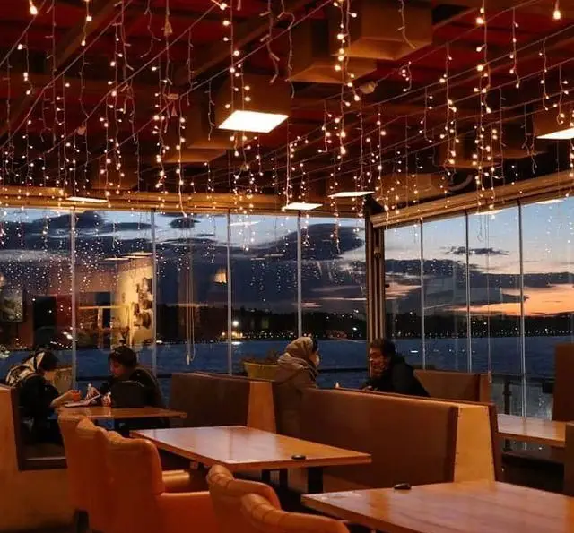 کافه رستوران رولینجا: فضایی دلنشین با دکوراسیون زیبا و چراغ‌های آویز، مشرف به منظره بی‌نظیر دریا و آسمان غروب. محیطی آرام برای مشتریان.