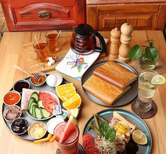 تصویری از میز صبحانه کامل و رنگارنگ کافه رستوران رولینجا با نان تازه، چای، آبمیوه، تخم مرغ، عسل، مربا، سبزیجات و مخلفات دلپذیر.