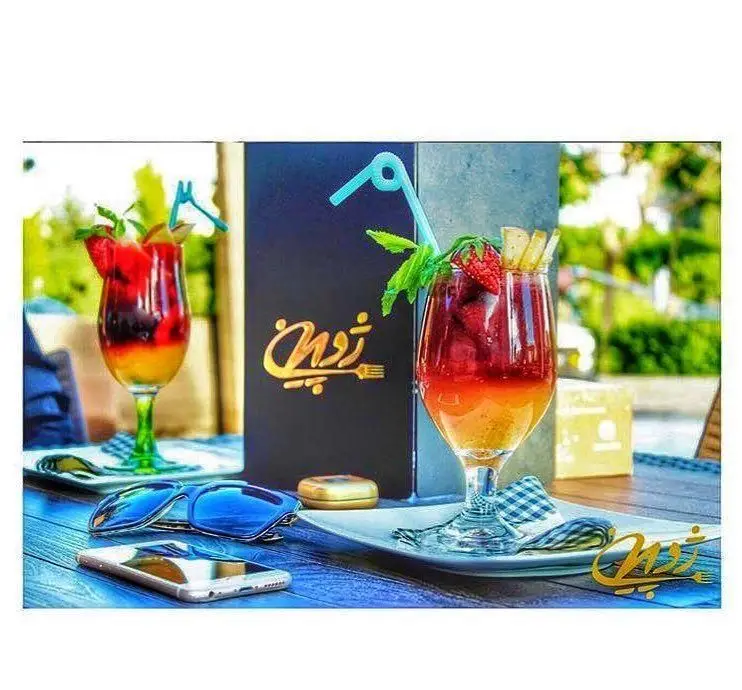 نوشیدنی‌های خنک و میوه‌ای رستوران ژوبین، شامل کوکتل و موکتل‌های رنگارنگ در فضای دلپذیر بیرونی با منو.