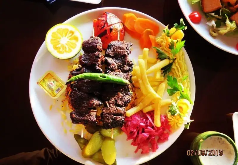 چلو کباب چنجه خوشمزه با سیب زمینی سرخ کرده، گوجه کبابی، خیارشور و لیمو در رستوران ژوبین. یک غذای اصیل و لذیذ ایرانی.