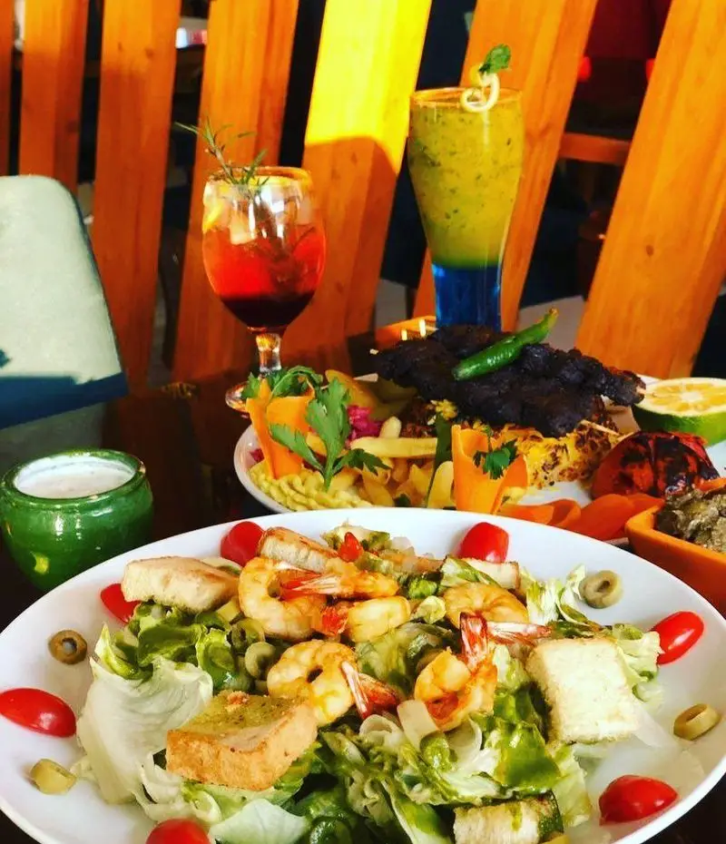 میز پر از غذاهای لذیذ در رستوران ژوبین: سالاد میگو تازه، کباب مخصوص، سیب زمینی سرخ کرده و نوشیدنی‌های خنک در فضایی زیبا.