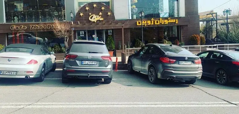 نمای اصلی و جذاب رستوران ژوبین و کافه ژوبین با تابلوی مشخص و خودروهای لوکس بی ام و، تیگوان و کیا پارک شده در جلوی ورودی.