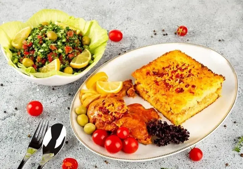 غذای انصار: یک بشقاب ته چین مرغ زعفرانی با سالاد شیرازی، زیتون و گوجه فرنگی گیلاسی. غذایی سنتی و خوشمزه برای ناهار یا شام.