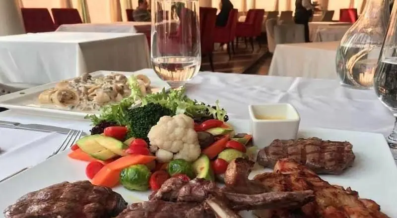 نمایی از میز غذای آماده سرو در رستوران ایرانی دروازه طهرون، شامل بشقاب میکس کباب و استیک با سبزیجات متنوع، به همراه پاستا در فضایی دلنشین و مجلل.