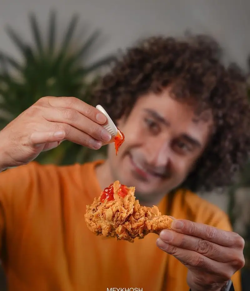 تجربه بی‌نظیر فست فود میخوش: مردی در حال افزودن سس به مرغ سوخاری کریسپی و طلایی خود برای لذتی وصف‌ناپذیر.