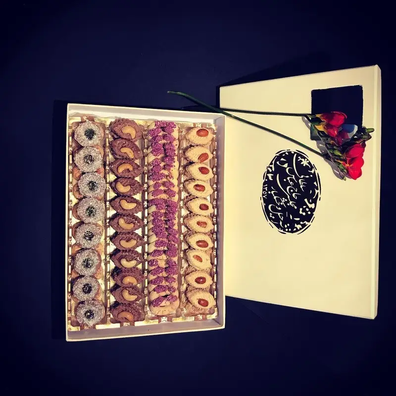 جعبه هدیه سوهان حاج عباس سلطانی با چیدمان چهار ردیف شیرینی متنوع: نارگیلی، شکلاتی مغزدار، ترافلی و بادامی، مناسب سوغات و پذیرایی.