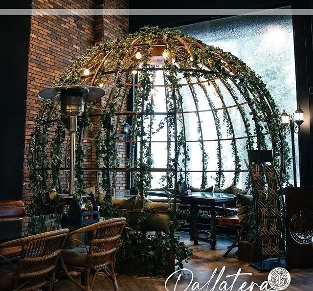 رستوران دالاترا: فضای داخلی دلنشین با گنبدی بزرگ و پوشیده از گیاهان سبز رونده، میز و صندلی‌های شیک، دیوار آجری و محیطی آرامش‌بخش.