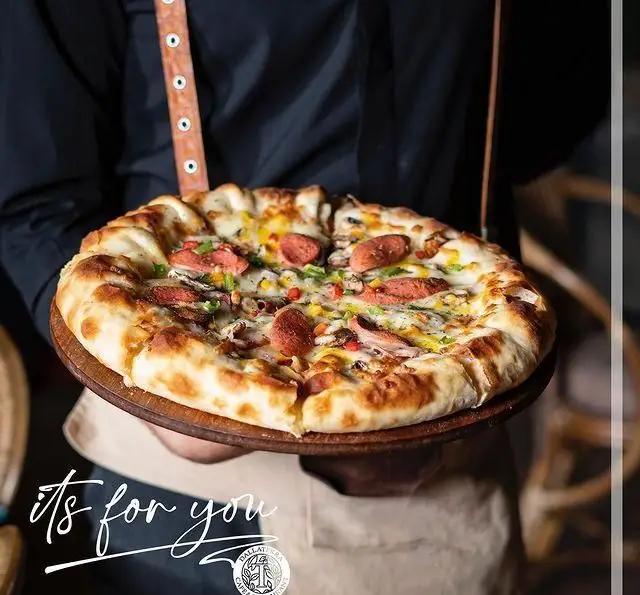 پیتزای تازه و داغ رستوران دالاترا با سوسیس، قارچ، ذرت و فلفل دلمه‌ای، سرو شده روی تخته چوبی. تجربه‌ای خوشمزه از دالاترا.