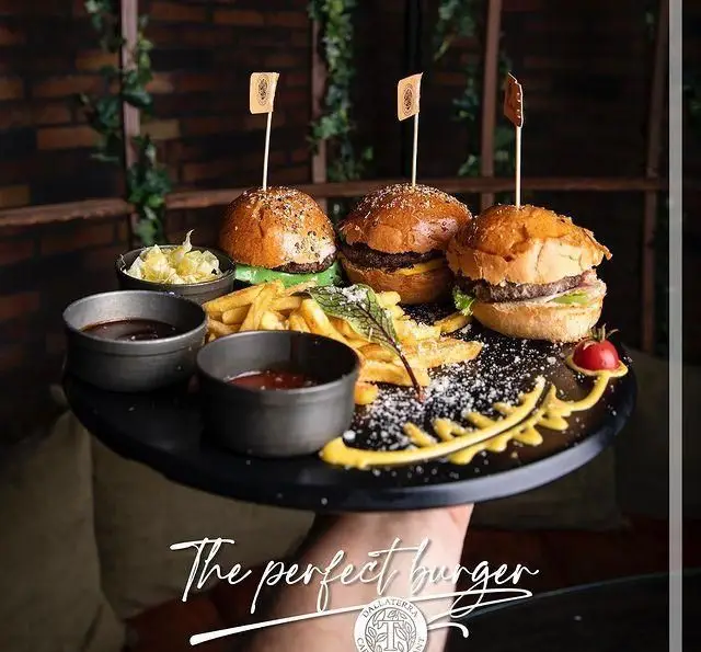 برگرهای عالی دالاترا: سه مینی برگر، سیب زمینی سرخ کرده و سس‌های لذیذ روی سینی مشکی در فضای دلنشین رستوران.