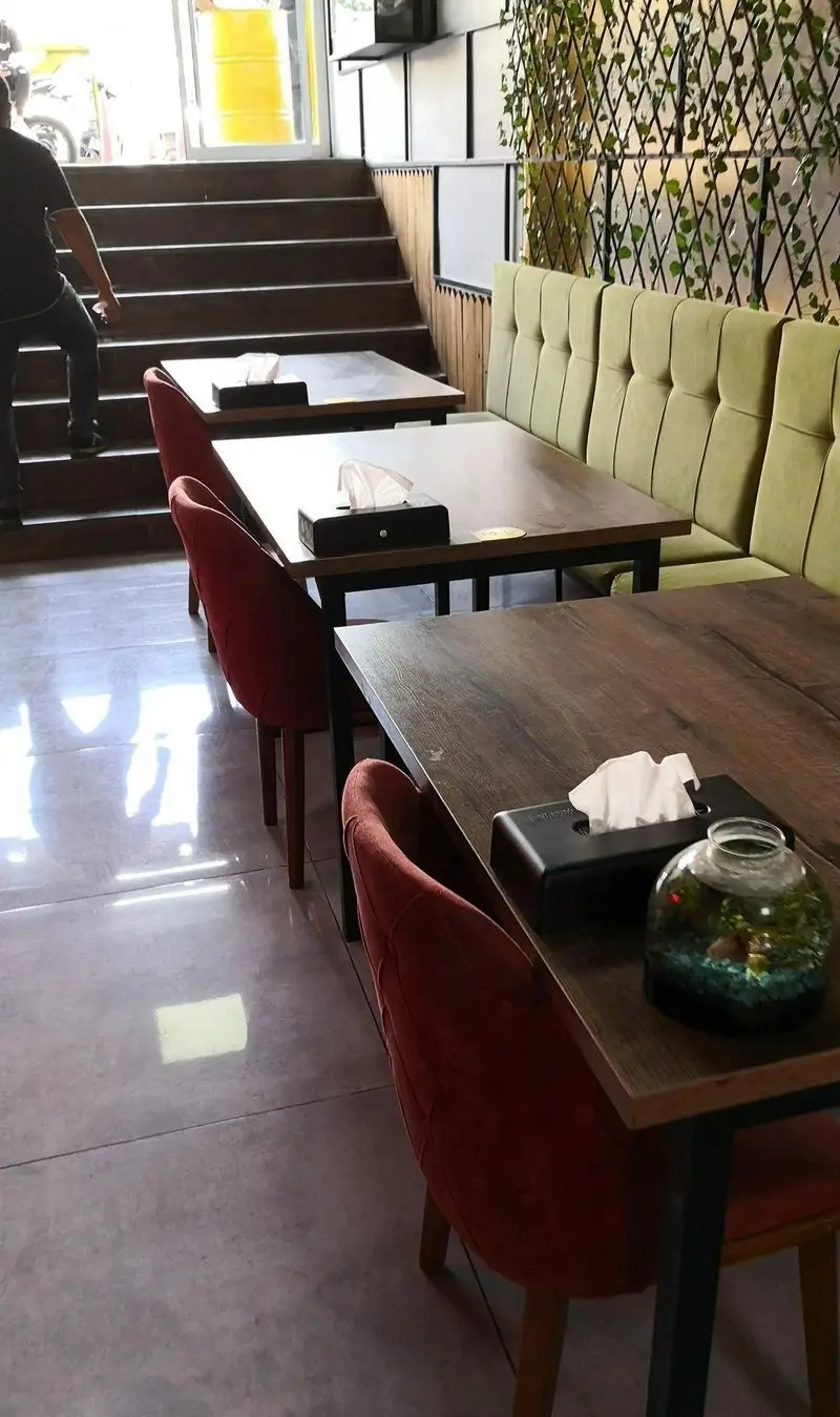 فضای داخلی مدرن فست فود لیرو با میزهای چوبی، صندلی‌های راحت قرمز و مبلمان سبز، دکوراسیون گیاهی جذاب و پله‌ها.