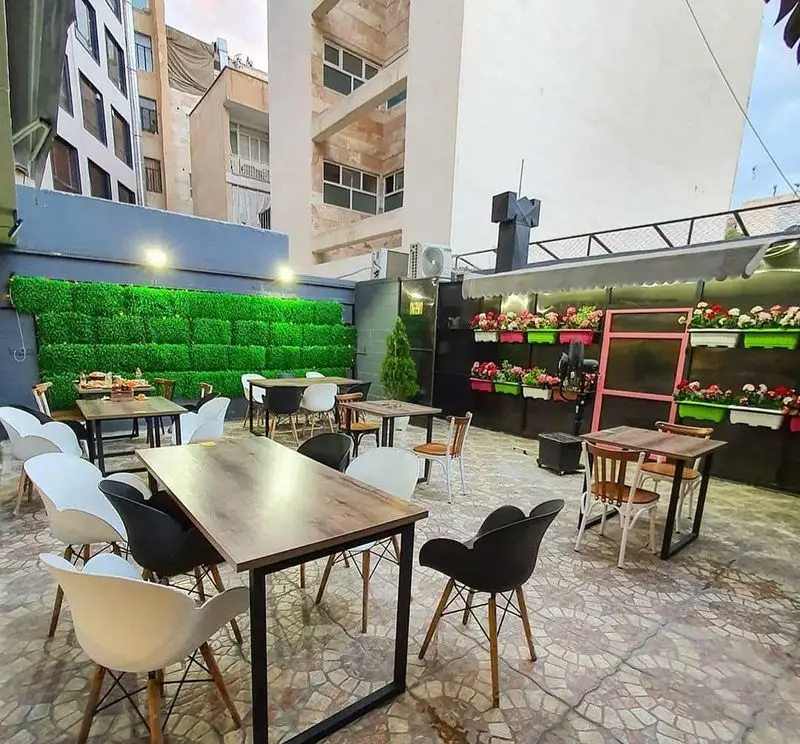 پاتیو دلپذیر فست فود لیرو با چیدمان مدرن میز و صندلی‌ها، دیوار سبز دکوراتیو و گل‌های شاداب، آماده پذیرایی از مهمانان.