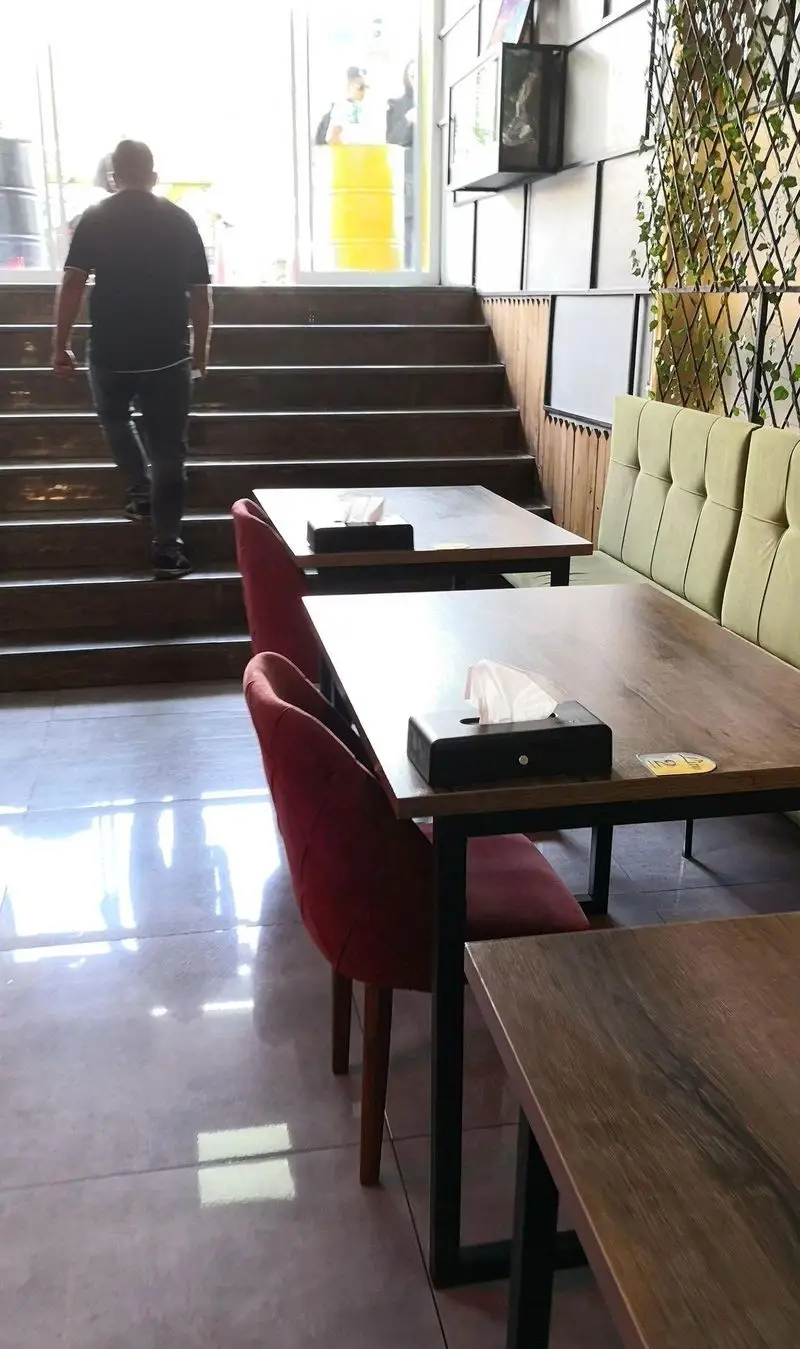 نمایی از محیط داخلی فست فود لیرو، شامل میز و صندلی‌های راحت، پله‌ها و دکوراسیون سبز و چوبی مدرن، ایده‌آل برای صرف غذا.