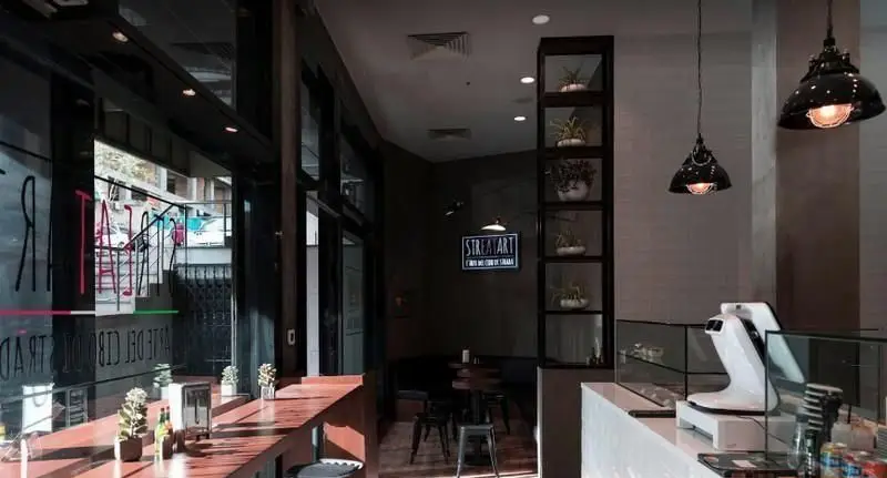 فضای داخلی دنج و مدرن پیتزایی استریت آرت با پیشخوان شیک، میز و صندلی چوبی، نورپردازی خاص و دکوراسیون جذاب.