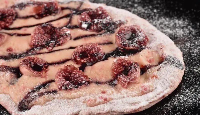 پیتزای دسر شیرین و وسوسه‌انگیز با توت‌های تازه، سس تیره شکلاتی و پودر قند، یک طعم هنری از پیتزایی استریت آرت.