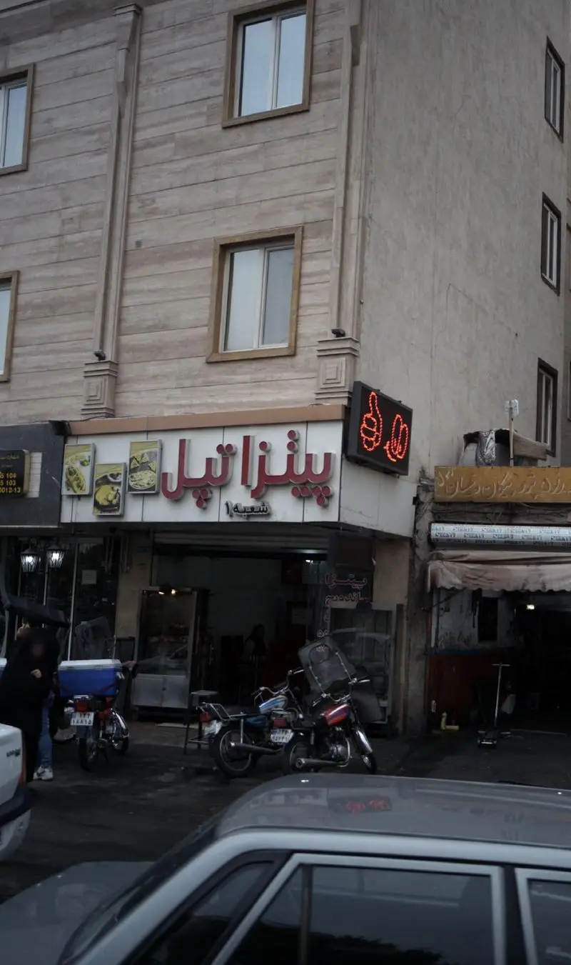 کسب و کار پیتزا تپل، رستوران فست فود با نمای سنگی زیبا، تابلو نئون چشمگیر و غذاهای خوشمزه، در محیط شهری شلوغ با وسایل نقلیه.