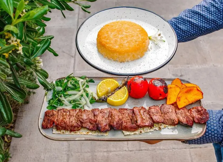 چلوکباب برگ لذیذ رستوران گیلانه با ته‌چین زعفرانی برشته، گوجه کبابی، سالاد پیاز و جعفری، لیمو و کدو حلوایی.