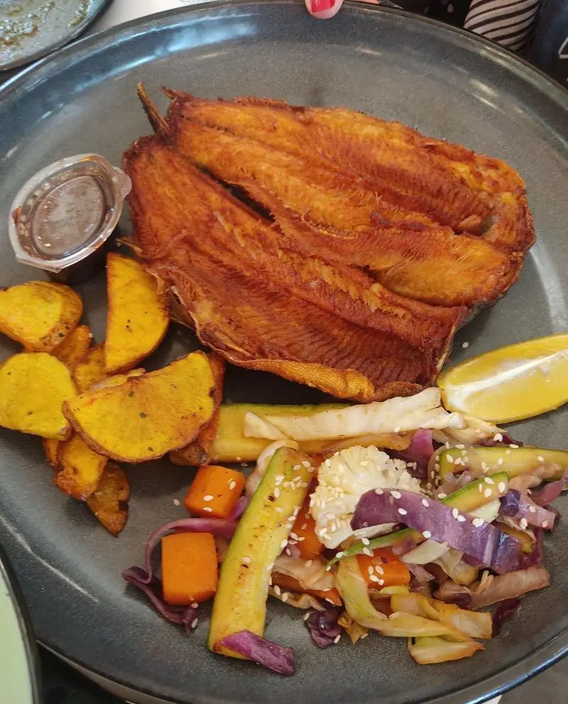 غذای لذیذ رستوران گیلانه: ماهی کامل سرخ‌شده با پوست طلایی، سیب‌زمینی برشته، و سبزیجات تازه شامل هویج، کلم و کدو.