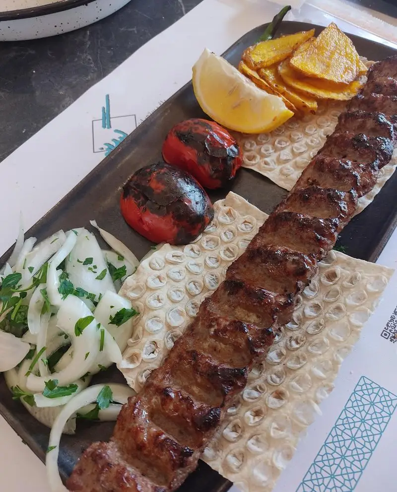 کباب کوبیده لذیذ رستوران گیلانه، همراه با گوجه کبابی، پیاز جعفری، لیمو و سیب زمینی سرخ شده روی نان داغ. غذای اصیل ایرانی.