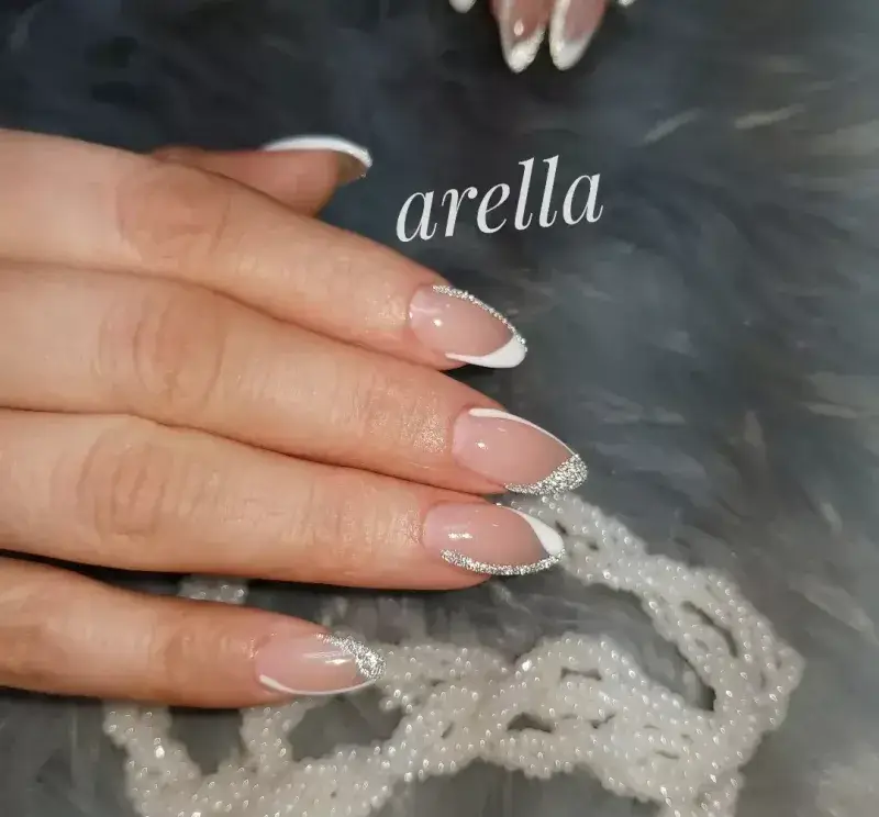 طراحی و کاشت ناخن شیک به سبک فرنچ با اکلیلهای نقرهای براق و لاک بیس نود روی ناخنهای بادامی شکل در سالن زیبایی آرلا