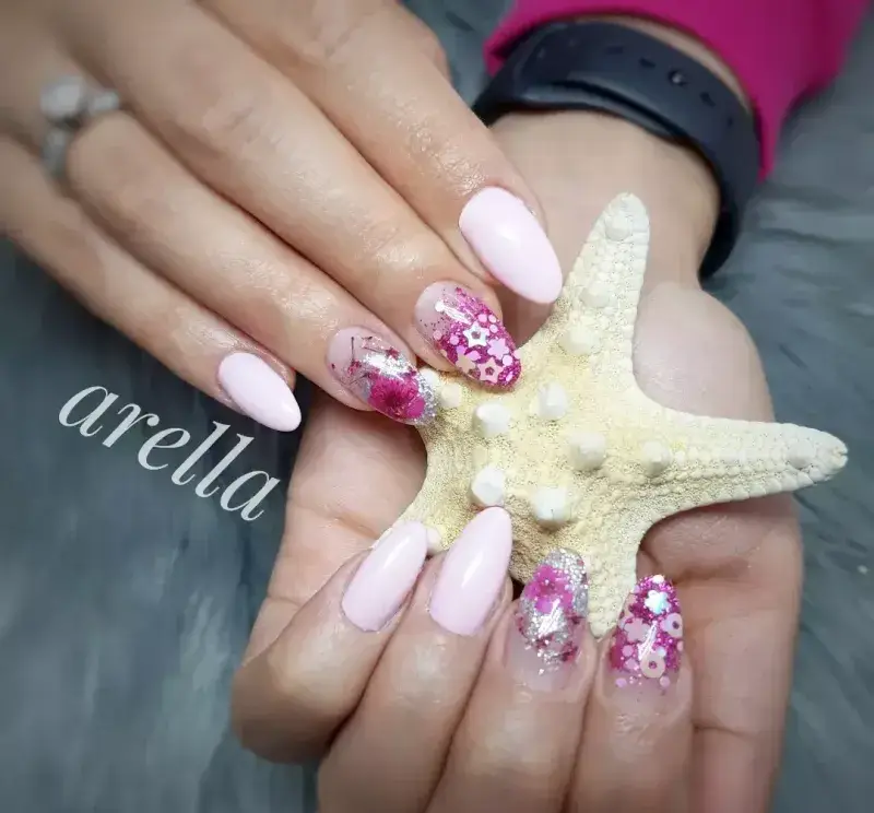 طراحی و کاشت ناخن شیک دخترانه با لاک صورتی ملایم و دیزاین اکلیلی ستارهای زیبا به همراه یک ستاره دریایی در دست