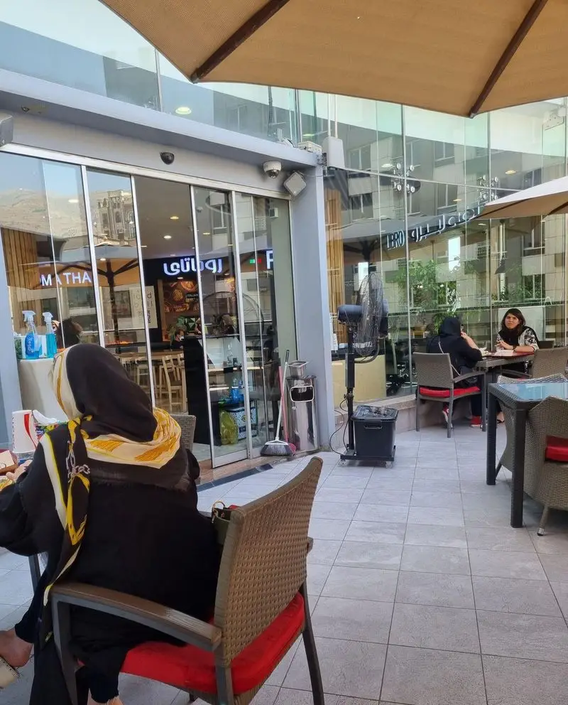 نمای فضای بیرونی دنج پیتزا کندیک با چترهای سایبان، مشتریان در حال لذت بردن از محیط آرام و صمیمی برای صرف غذا و نوشیدنی.