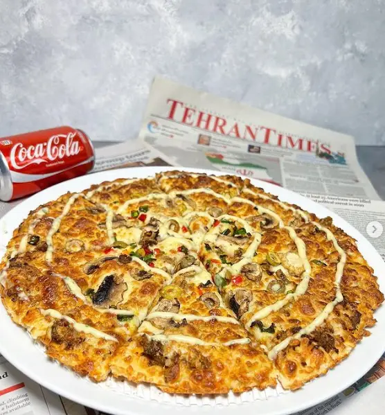 پیتزا کندیک: پیتزای قارچ و پنیر طلایی با سس دلپذیر، همراه با نوشابه کوکاکولا خنک و روزنامه تهران تایمز در پس زمینه.