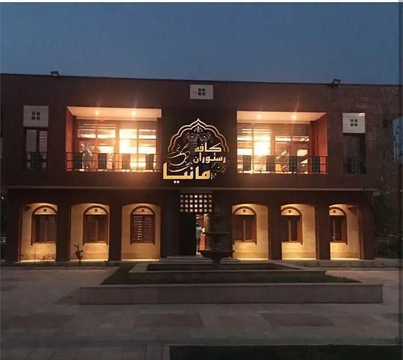 نمای خارجی کافه رستوران مانیا در شب با نورپردازی گرم و دلنشین. معماری مدرن و شیک ساختمان، مکانی ایده‌آل برای صرف غذا و نوشیدنی.