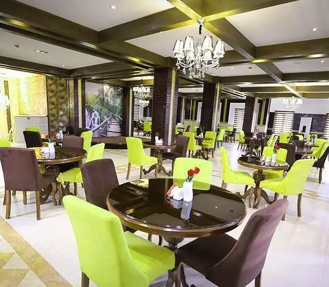 نمای داخلی دنج و مدرن کافه رستوران مانیا با چیدمان میز و صندلی‌های سبز و قهوه‌ای، مناسب برای وعده‌های غذایی و دورهمی.