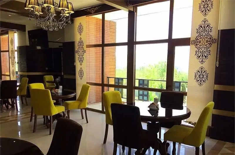 دکوراسیون شیک کافه رستوران مانیا با لوستر مجلل، میز و صندلی‌های راحت و پنجره‌های بزرگ رو به طبیعت سرسبز.