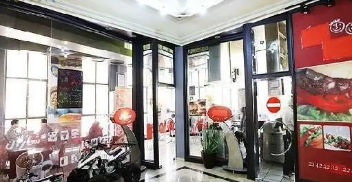 عکس نمای بیرونی فست فود شاران با درب‌های شیشه‌ای و پوسترهای بزرگ تبلیغاتی از غذاهای لذیذ مانند برگر و سالاد.