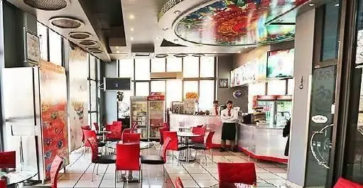 نمای داخلی شیک و مدرن فست فود شاران با میز و صندلی‌های قرمز، پیشخوان پذیرایی و سقف رنگارنگ، محیطی جذاب برای مشتریان.