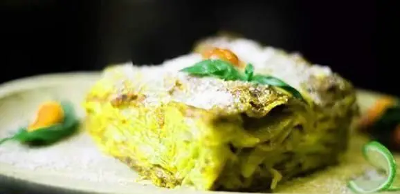برش چشم نواز لازانیا سبز با لایههای جذاب، روی آن پنیر پاشیده و برگ ریحان تازه، از منوی خوشطعم کافی شاپ تومو.