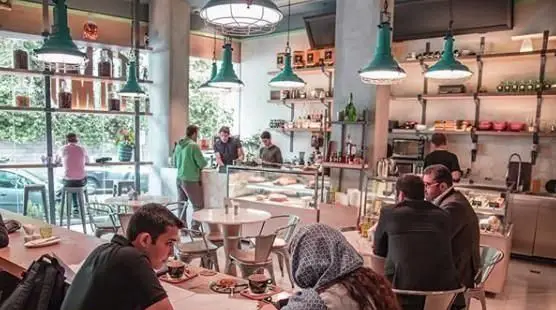 نمایی از داخل کافی شاپ تومو: مشتریان در حال استراحت و نوشیدن قهوه، باریستاها در حال آمادهسازی سفارشات در فضای دلپذیر و مدرن.