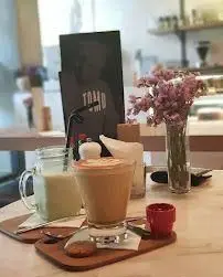 میز چوبی در کافی شاپ تومو با لاته، نوشیدنی سرد، کوکی و گلهای بنفش. محیطی آرام و دلنشین برای لذت بردن از قهوه و ملاقاتها.
