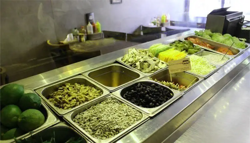 پیشخوان سالاد بار برگر بار با مجموعه‌ای کامل از تاپینگ‌های تازه شامل کاهو، زیتون، قارچ و آجیل برای ساندویچ و سالاد.